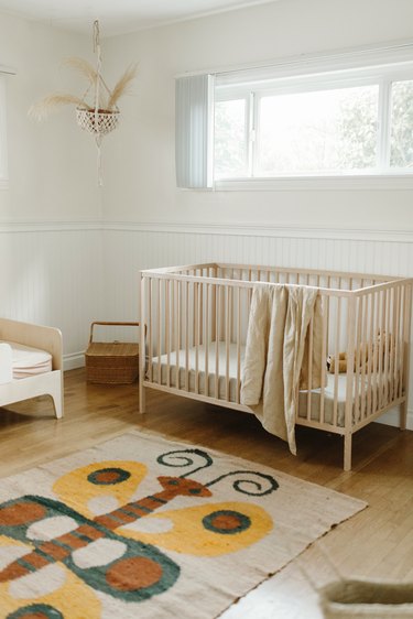 Neutral wood and white nursery with crib and butterfly rug on wood floor