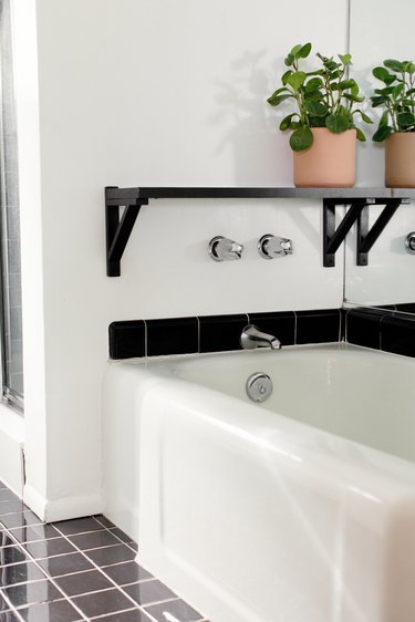 Black shelf with plant over white tub