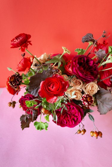 a diy floral centerpiece made of caramel roses and red flowers  including ranunculus and zinnias