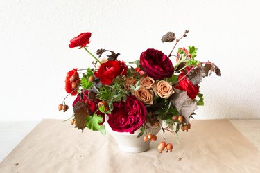 A DIY floral centerpiece made of caramel roses and red flowers, including ranunculus and zinnias