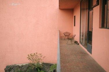 Pink Mid-Century building exterior with large windows and chairs on a brick walkway
