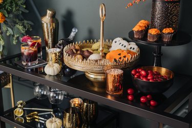 fall party idea with bar cart and gold cocktail set and cake stand with halloween cookies