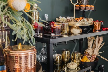 Bar cart with gold cocktail set and cake stand decorated with flowers, pumpkins and corn