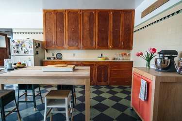 Kitchen with wood cabinets and dining table, stools, walls with beige tiles and triangle accent tiles, a portable cabinet with pink doors.