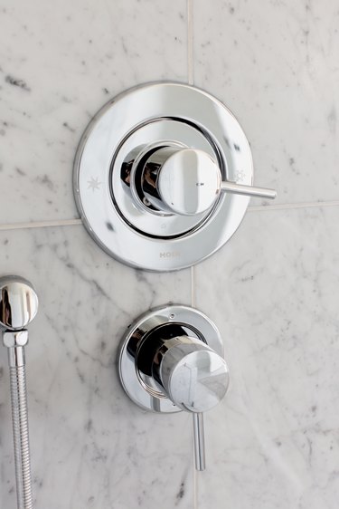 Silver shower faucets handles mounted on a granite or marble tile wall.
