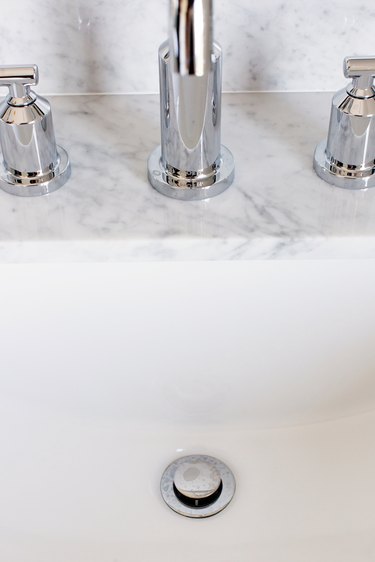 A sink with a silver faucet and drain. The countertop is marble or granite.
