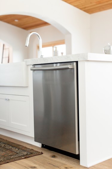 Stainless steel dishwasher in a white kitchen island. The marble countertop extends over the dishwasher. A chrome faucet is visible.