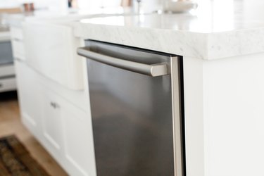 Stainless steel dishwasher in a white kitchen island. The marble countertop extends over the dishwasher.