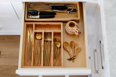 An open cutlery drawer with a wooden organizer, cold cutlery, and various other utensils.