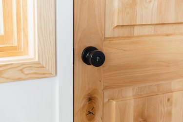Closeup of a wooden door with a black doorknob. The corner of a light wood window frame is visible.