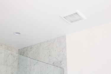 A bathroom ceiling vent above a glass shower door