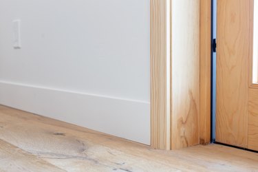 Wood floor near a door. The bottom of a wooden door frame next to a white wall with white trim.