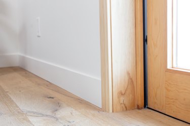 Wood floor near a door. The bottom of a wooden door frame next to a white wall with white trim.