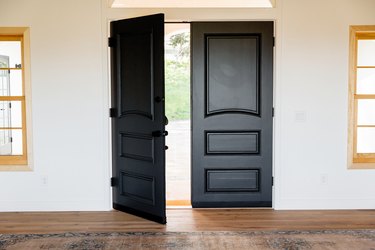 Double doors made of dark wood, the main entrance to the home. Two windows with light wood frames, one on either side of the door.