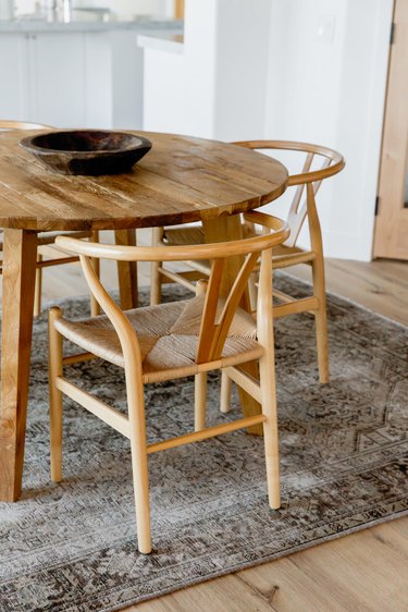 A round wood dining table with two chairs on a grey patterned rug.