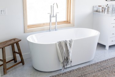 A freestanding garden tub in a white bathroom next to a wooden stool