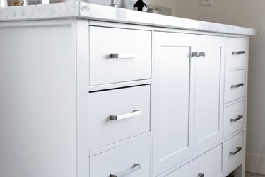 A white bathroom vanity with drawers of varying sizes and thin silver bar handles.
