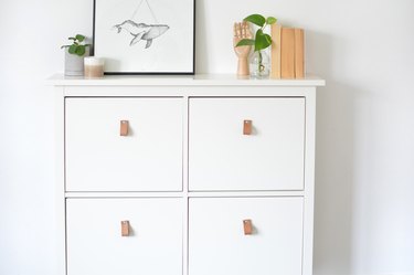 White dresser with leather pull handles on drawers with art and plants