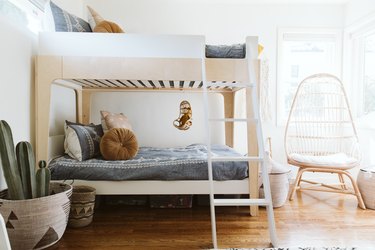 A kid's room with a bunk bed, blue bedding, neutral pillows, Boho rattan chair, and baskets.