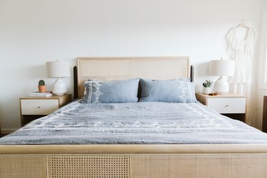 Bedroom with a cane headboard, blue bedding, wood nightstands with white drawers, cacti, and white lamps.