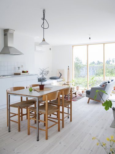 a simple wooden dining table and wooden chairs on a light wood floor in a bright white kitchen
