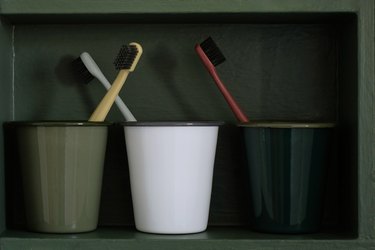 Green and white cups with toothbrushes in forest green cabinet