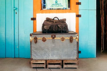 a leather duffel sits on top of a vintage steamer trunk outside a hotel