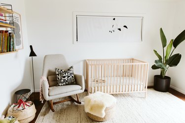 Nursery with gray rocking chair, black floor lamp, wood crib, sheepskin throw, fiber accents, Calder mobile, and plant