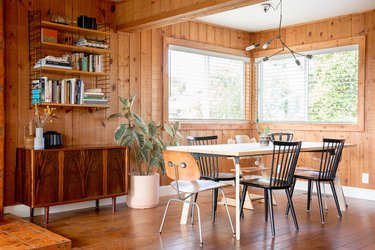 Wood walled dining room with bulb chandelier, eclectic chairs, wood dining table, plant, wood bookshelves, and credenza