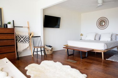 Minimalist bedroom with sheepskin throws, wood bed frame, round sunburst mirror, and wood furniture.