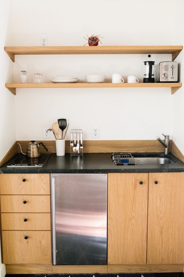 kitchenette with light wood cabinets, black counters, two shelves, a mini fridge, and small stovetop