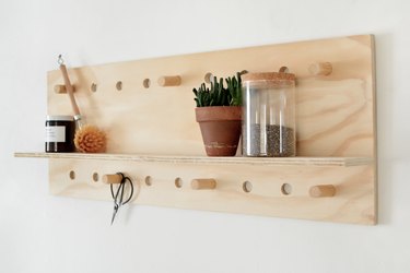 a shelving unit hung on a wall made from a plywood sheet with a shelf glued on a many holes drilled for pegs made from thick wooden dowel