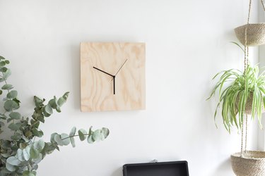 A clock with an unfinished plywood face mounted on a plain white wall.