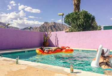 Exterior pool with lobster and swan inflatables, pink-painted brick walls, and tan patio against clouds and mountain