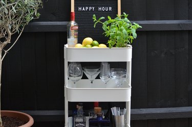 White bar cart with liquor bottles, glasses, and plant
