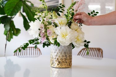 Hand placing white and pink flowers in a vase with green leaves