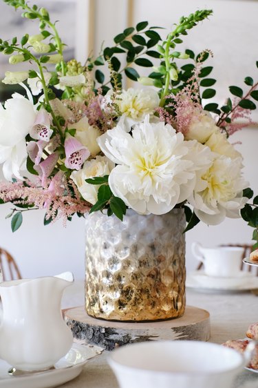 Gold-white textured vase with white and pink flowers with foliage on dining table