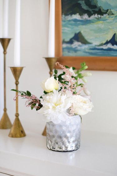 Vase of white and pink flowers on white counter with gold candlesticks and painting