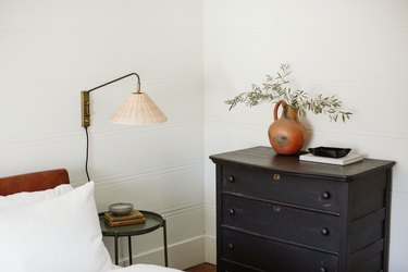 round bedside table, lamp, black dresser and orange vase