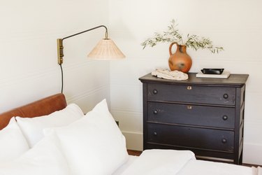 round bedside table, lamp, black dresser and orange vase