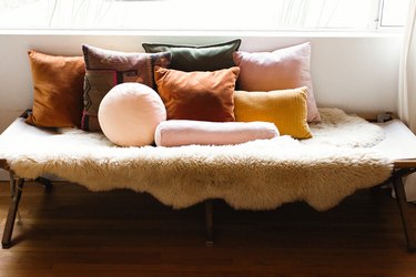 A bench with colorful pillows and a sheep throw blanket.