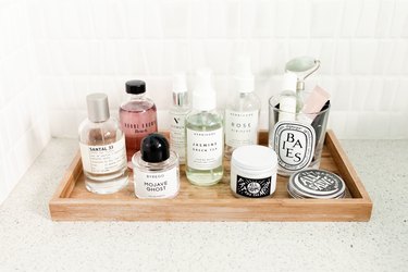 A wood tray with bottles of 'Beyredo', 'Bobbi Brown', 'Herbevore', 'Santal 33', 'Fat and the Moon', and a 'Diptyque' candle.