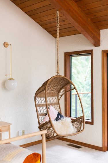 A woven boho chair, hanging from a wood beam ceiling, and a globe sconce.