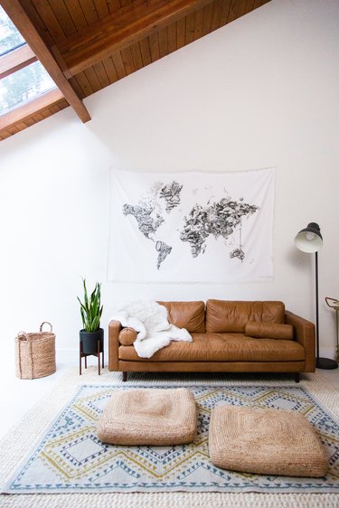 Living room with world map tapestry, leather sofa, sheep throw, snake plant, woven accents, wood ceiling.