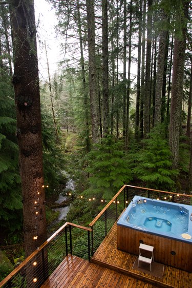 A jacuzzi on a wood deck, with string lights. Forrest trees surround.