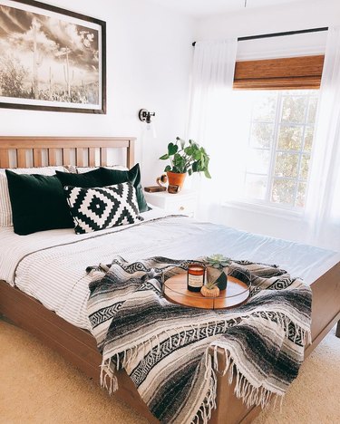 Minimal southwestern-inspired bedroom with black and white mexican blanket and dark green velvet throws on white bedding