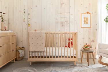 Gender-neutral nursery featuring wood dresser, crib, and paneling, a stool, and a woven hamper