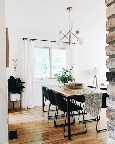 Minimal dining room with metal and wood table and black leather industrial chairs, white globe chandelier, and white midcentury floor planter