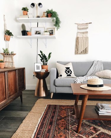 Southwestern-boho living room corner with gray mid-century couch and wooden mid-century coffee table, plus red persian rug layered atop jute rug