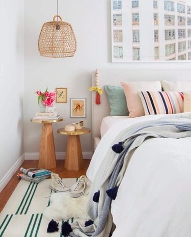White bedroom with pastel throw pillows and woven bell-shaped pendant light